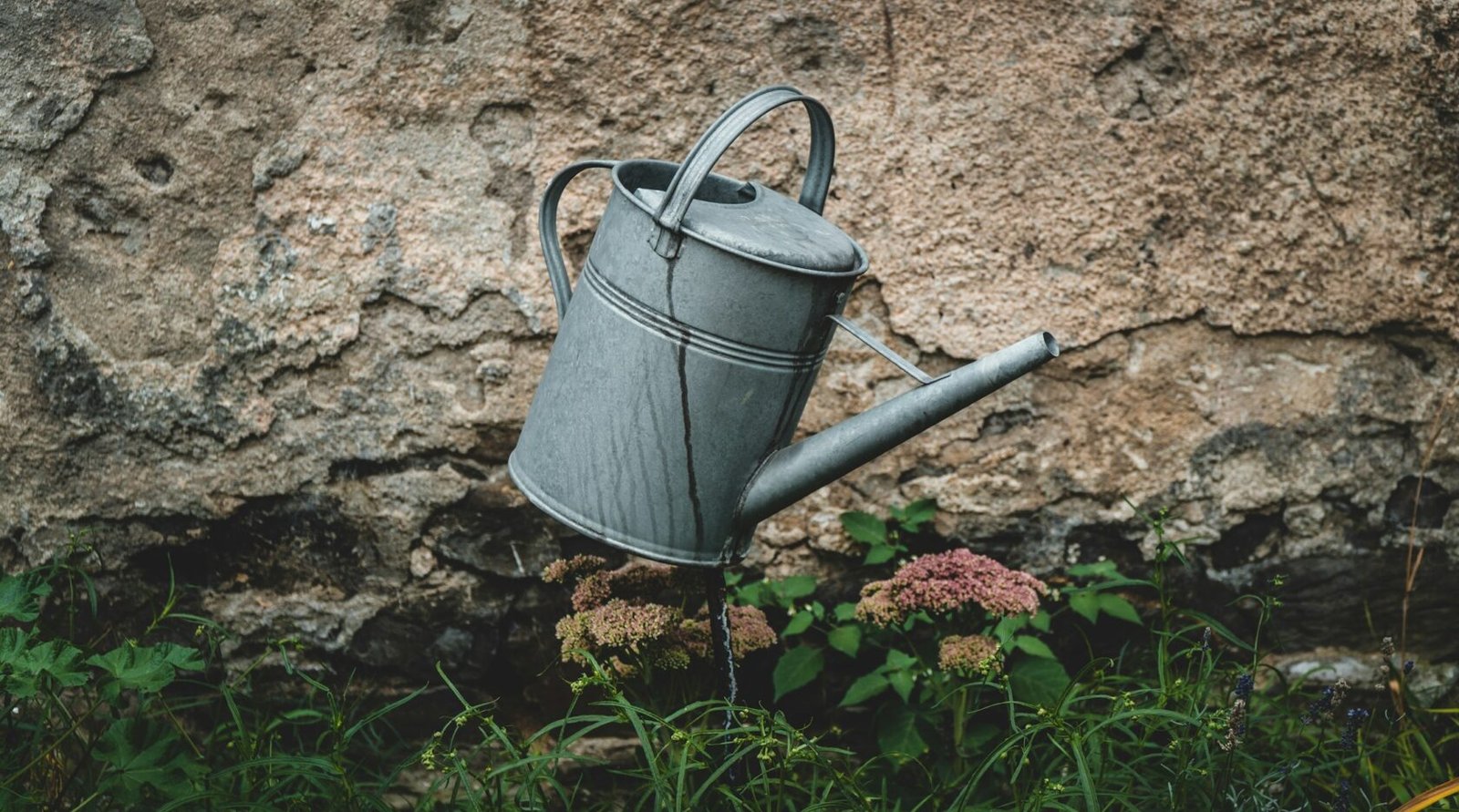 A watering can pouring water directly onto already-saturated brown soil
